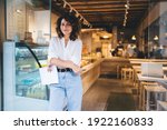Small photo of Half length portrait of prosperous manager of local bakery smiling at camera during work day in franchise takeaway cafe, happy woman with paper statistics enjoying time for improve own coffeehouse