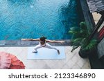 Small photo of Top view of woman in track suit stretching in yoga pose breathing - enjoying recreation at patio pool terrace, Caucasian female practice yoga feeling balance in asana keeping body shape in tonus