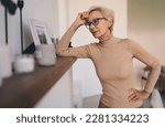 Small photo of Exalted slim aged lady wearing casual clothes leaning on shelf at home while reminiscing past years and looking at old photo in frame