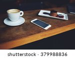 Close up of mobile phone lying on a wooden table near cup of cappuccino and plate of sweet dessert in coffee shop interior, leisure time concept, rest in cafe
