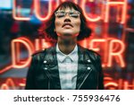 Trendy and stylis young woman in eyeglasses closed eyes enjoying in big city atmosphere in nigh, cool dressed hipster girl in spectacles with illumination reflection standing against nightlights