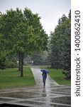 Small photo of OBERLIN, OHIO / USA - SEPTEMBER 5 2009: Oberlin student under a blue umbrella walks through main quad at Oberlin College.