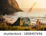 Camping with tent in Lofoten islands, Northern Norway, Kvalvika beach, during sunset. Person sitting in front of tent.