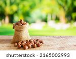 Small photo of Hazelnuts, filbert in burlap sack and in brown bowl on wooden table. heap or stack of hazelnuts. in front of the background of trees