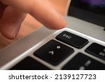 Hand pressing escape key on modern laptop keyboard. Esc sign and symbol closeup