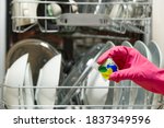 Dishwasher Detergents in hands. hands in pink golvs holds dishwasher gel capsules. Capsule for the dishwasher. Brilliant cleanliness.