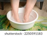 Small photo of Foot soaking. Woman put hot water for her feet. Homemade bath soak for dry feet skin. Female feet with spa bowl.
