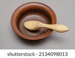 Small photo of Brown earthenware bowl and buckshot against a gray background. Empty bowl and billet for carving a wooden spoon. Selective focus.