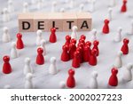 Small photo of wooden blocks with the word delta surrounded by white and red wooden figurines. symbol for corona mutant delta.