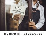 Small photo of Store owner turning close sign broad through the door glass for social distancing prevent corona virus outbreak.