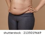 Small photo of Front view of overweighted thick belly of woman wearing leggings. Body positive. Violation of cell elasticity, loss of nutrients. Sagging skin after pregnancy or sudden weight loss.
