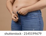 Small photo of Overweighted lady with large abdomen in process of zipping up blue jeans. Sudden weight gain. Visceral fat. Body positive. Tight little clothes. Need for wardrobe change.