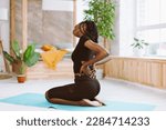 Small photo of African American multicultural sportswoman with dreadlocks stretching, inclining, do yoga. Female holding back, feeling pain in joints and muscles, backache. Health and body care. Side view