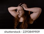 Small photo of Young upset woman rending long hair. Female portrait isolated on black, side view. Shouting and screaming loud with open mouth. Feelings, pain, suffering. Human emotions, facial expression concept.