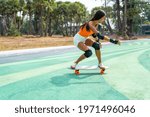 Attractive Asian woman with safety skateboarding knee pad skating at skateboard park by the beach. Happy female enjoy summer outdoor active lifestyle play extreme sport surf skate at public park.