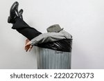 Small photo of Portrait of Businessman in Suit and Fedora Hat Sitting in Trash Can. Man Thrown Away by Capitalism and Greed.