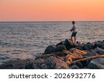 Active recreation in nature. A man with a fishing rod is fishing on the rocks near the sea. A fisherman catches fish at sunset.