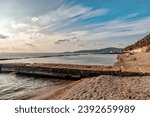 Small photo of View of the sea breakwater made of stones. Seascape at sunset under a cloudy sky. Waves on the sea and dark clouds in the blue sky. A beach with a breakwater made of large stone boulders.