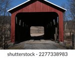 Small photo of Historic Frazier red wooden covered bridge over Little Muncy Creek in Lycoming County Pennsylvania built in 1888 against blue cloud sky. You can drive through it today. Built in the Burr Arch style.