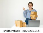 Small photo of Young Asian woman business owner with many parcel boxes on the table happy online sales job, use the laptop, get an order from customers, take notes, and make arrangements for delivery by post.