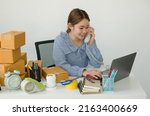 Small photo of Young Asian woman business owner with many parcel boxes on the table happy online sales job, use your laptop, get an order from customers, take notes, and make arrangements for delivery by post.