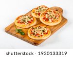 Open small pies, mini pizzas with sausage, pickles, tomatoes, mozzarella, parsley, greens on a wooden board on a white background 