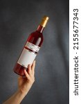 Small photo of Male hand holding bottle of pink red wine, natural fruit alcohol liquor with empty label on grey background. Mock up, template for brand, vertical shot