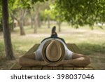 Restful young man wearing a straw hat laying down on a wooden table in the middle of the forest at a park