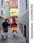 Small photo of Bremen, Germany - 2014: German Fussball (soccer or football) fan walks down Bottcherstrasse (Cooper's Alley) before a big game. Lichtbringer ("Bringer of Light") by Hoetger hangs above the entrance.