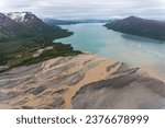 Ukak River flows into liuk Arm Naknek Lake in Katmai National Park, Alaska. Aerial view of river tan with suspended ash from Valley of Ten Thousand Smokes empties into glacial blue fresh water lake. 