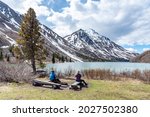 Hikers resting, sitting beside a isolated St Elias Lake in Kluane National Park during spring time, May with no other people. Snow capped mountains surrounding the scenic, Canadian view.