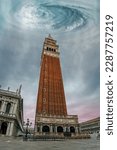 Small photo of Low angle view of the Campanile bell tower on St. Mark's square in center of Venice under dramatic cloudy sky with huge storm vortex, Italy. Scary apocalyptic scene