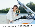 An annoyed and angry woman, near a broken car, tries to call an insurance agent and a repair crew. for car repair