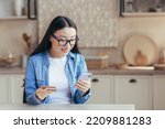 Young asian woman happily shopping online sitting at home in the kitchen, woman using smartphone and bank credit card for online shopping