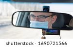 Small photo of Coronavirus. A young male driver is sitting in a car wearing a medical mask. view of the rear view mirror of the car. self-defense against the virus
