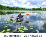 woman enjoying weekend rowing on transparent boat in small lake, bright sunlight, cloud reflections, sunny summer day