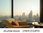 A chair and table with a wine glass in hotel room with Bangkok City skyline in Thailand. Financial district and skyscraper office buildings. Downtown skyline. Urban town. Relaxing area. Lifestyle.