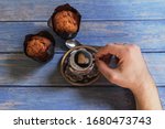 Male hand holds a cup of black coffee with foam in the shape of a heart and vanilla muffins on a background of blue wooden table