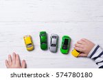 Child hands playing with miniature toy cars, wooden background, top view