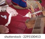 Small photo of Close up hands of a woman feeds cotton wool into wooden bobbin, traditional spinning wheel to make yarn. Detail of thread, spinning cotton in traditional way
