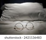 Small photo of An eyeglasses optics on white linen bed, low light night time, shortsighted, nearsighted, farsighted, eyewear business products, relax or rest or sleeping time concept, focus on foreground