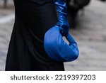 Small photo of Milan, Italy - September, 21, 2022: Street style outfit details, woman wearing black long skirt, corset, blue leather gloves and leather shiny electric blue handbag. Woman holding bag
