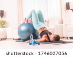 Young girl holds legs on a fitness ball lifting her whole body with elbows on the floor. Home workout using a mat, dumbbells and a swiss ball.