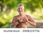 Old but fit man with grey hair shows a heart gesture with his fingers as a sign of his healthy cardiovascular system.