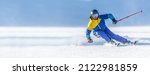 Small photo of A young aggressive skier on an alpine slope demonstrates an extreme carving skiing style. He is skiing on morning perfectly groomed piste.