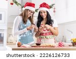 A mother and her teenage daughter dressed in Christmas aprons are making Christmas cookies at home in the kitchen.