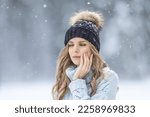 Small photo of A young woman has a toothache outside in winter weather, she has sensitive enamel to the cold.