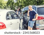 Small photo of Man and woman, who had a car incident resulting in scratched cars are both calling on their phone for police, insurance and assistance.