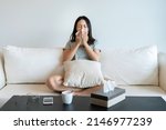 Small photo of Sick young Asian woman sitting on couch blowing her nose on a tissue conceptual of healthcare , seasonal flu, rhinitis or an allergic reaction in hay fever.