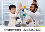 Small photo of A high-five boy with a teacher in a science classroom at an elementary school using a Joule telescope. The enthusiastic teacher explains chemistry to children, and children learn with interest.
